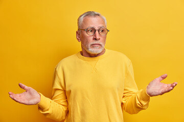 Portrait of puzzled hesitant bearded mature man spreads palms and faces difficult choice looks...