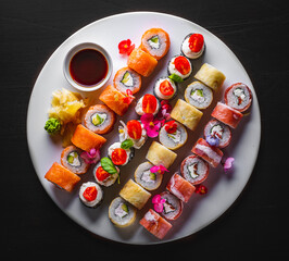 set of sushi roll with salmon, avocado, cream cheese, cucumber, rice, caviar, eel, tuna in white plate on black wooden table
