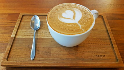 Weiße Tasse mit Kaffee und Latte Art Milchschaum auf Holztablett mit silbernem Löffel und Wort...