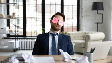 Tired sleepy businessman with stickers, adhesive notes on eyes sleeping at workplace, sitting at work desk in office, unproductive lazy employee executive dozing, working on difficult project