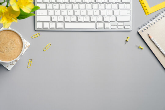 Flat lay top view yellow office supplies, flower, keyboard, cup of coffee on grey desk table. Modern freelancer workspace in minimal style.