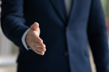 Close up businessman wearing suit extending hand for handshake to business partner or customer at meeting, hr manager greeting candidate at job interview, first impression or acquaintance