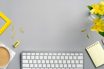 Flat lay top view office desk table. Workspace with computer keyboard, coffee cup, yellow stationery and flower on grey background. Freelancer workplace in minimal style.
