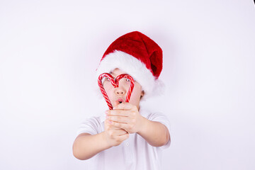 a boy in a Santa Claus hat holds Christmas candies on a white background