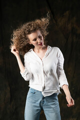 A beautiful girl, wearing jeans and a blouse, poses cheerfully in the wind, which blows her long curly hair and clothes. Advertising, commercial design