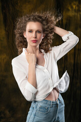 A beautiful girl, wearing jeans and a blouse, poses cheerfully in the wind, which blows her long curly hair and clothes. Advertising, commercial design