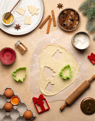 Process of making Christmas cookies with homemade dough,cookie cutters in the shape of tree and gift box,rolling pin,flour,cinnamon,cocoa powder and fresh eggs on beige table.Top view.