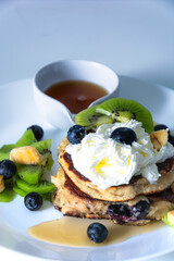 Almond flour pancake decorated with blue berries , maple syrup and vipped creame served on white plate