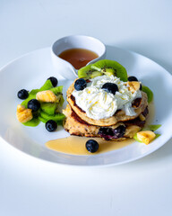 Almond flour pancake decorated with blue berries , maple syrup and vipped creame served on white plate