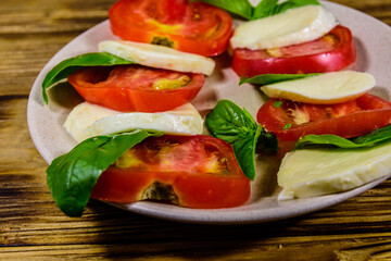 Plate with caprese salad (italian salad with cherry tomatoes, mozzarella cheese and basil leaves) on wooden table