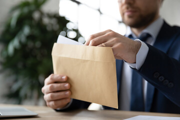 Close up businessman wearing suit holding opening paper envelope with letter in office, sitting at desk, working with correspondence, executive employee received news or important information - obrazy, fototapety, plakaty