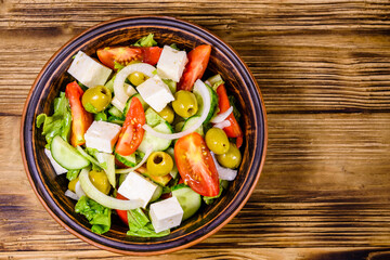 Ceramic plate with greek salad on wooden table. Top view