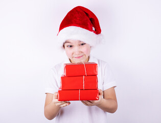 A cute child in a Santa hat holds a red gift box with a craft ribbon isolated on a white background