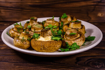 Plate with baked champignons, dill and parsley on a wooden table