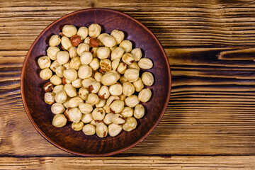 Ceramic plate with peeled hazelnuts on a wooden table. Top view