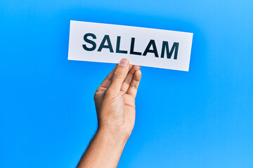 Hand of hispanic man holding sallam word paper over isolated blue background.