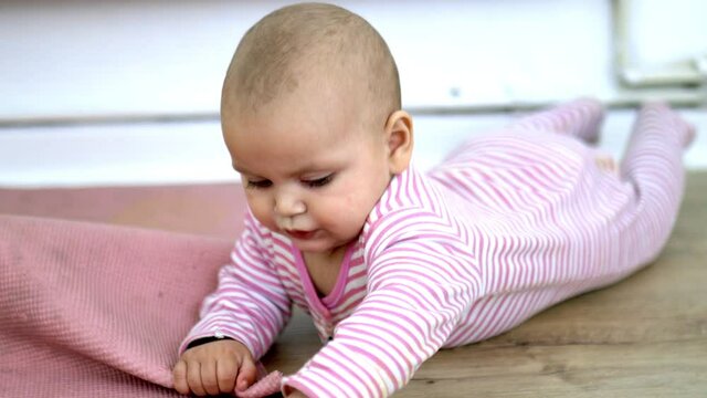 Adorable baby lying on the wooden floor and playing with a pink mat