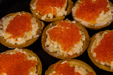 Tartlets with red caviar on a black plate. Festive food
