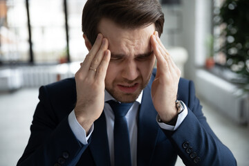 Close up stressed businessman wearing suit touching temples, suffering from strong headache,...