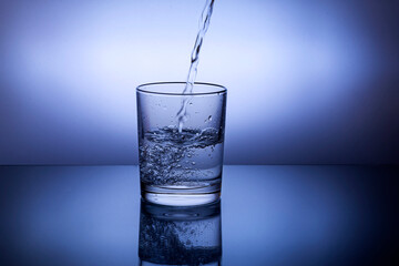Pouring water into a glass against the blue background