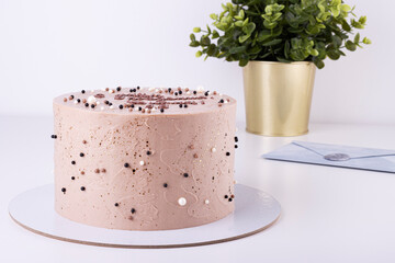 Chocolate cream cake on a white backing with beads, green plant with a blue envelope in the background