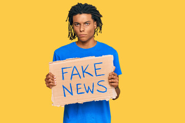 Young african american man holding fake news banner thinking attitude and sober expression looking self confident