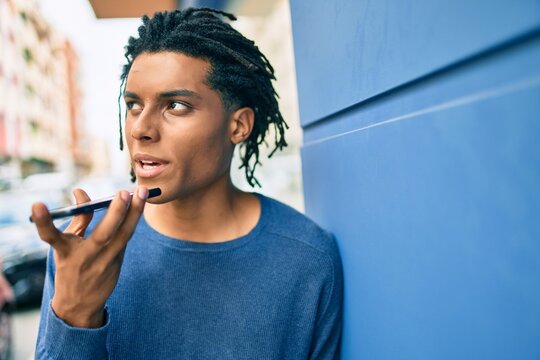 Young african american man with unhappy expression sending audio message using smartphone at street of city.