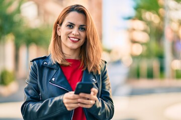 Young latin woman smiling happy using smartphone at the city.