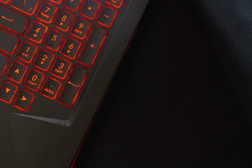 Obraz premium Laptop keyboard with red backlight on a black mouse pad. Background. Copy space.