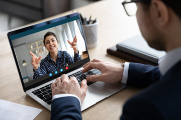 Close up businessman chatting online with Indian businesswoman colleague, looking at laptop screen,...