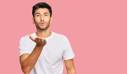 Young handsome man wearing casual white tshirt looking at the camera blowing a kiss with hand on air being lovely and sexy. love expression.