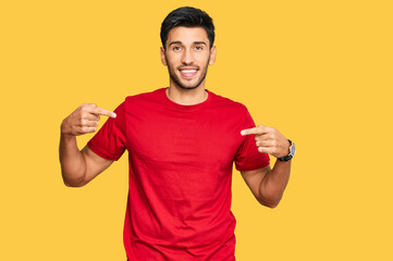 Young handsome man wearing casual red tshirt looking confident with smile on face, pointing oneself with fingers proud and happy. - obrazy, fototapety, plakaty