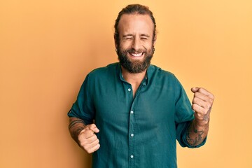 Handsome man with beard and long hair wearing casual clothes celebrating surprised and amazed for success with arms raised and eyes closed