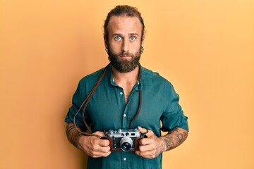 Handsome man with beard and long hair holding vintage camera relaxed with serious expression on face. simple and natural looking at the camera.