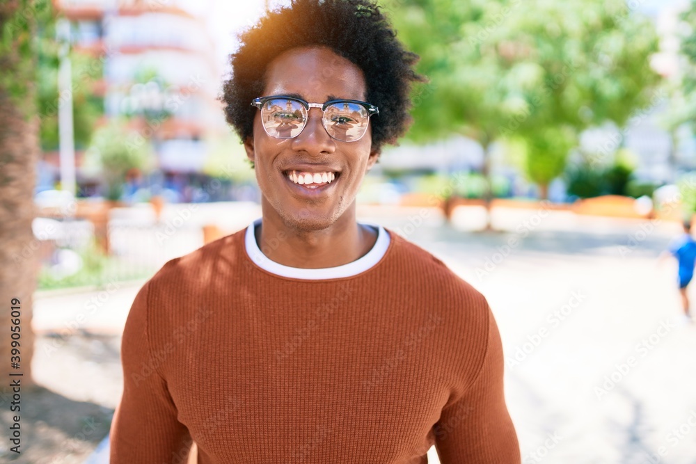 Wall mural Young handsome african american man wearing casual clothes and glasses smiling happy. Standing with smile on face looking to the camera walking at town street.