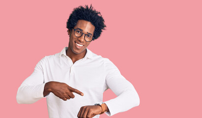 Handsome african american man with afro hair wearing casual clothes and glasses in hurry pointing...