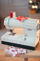 Mother's home workshop for sewing and tailoring. christmas patterned face masks lying on a sewing machine. DIY and handmade