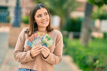 Young hispanic woman smiling happy holding australian dollars at the city.