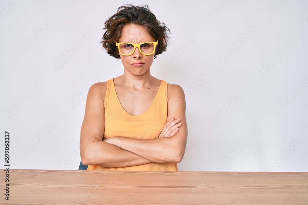 Sticker Young hispanic woman wearing casual clothes and glasses sitting on the table skeptic and nervous, disapproving expression on face with crossed arms. negative person.