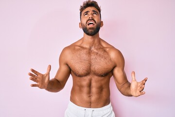Young hispanic man standing shirtless crazy and mad shouting and yelling with aggressive expression...