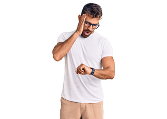 Young hispanic man wearing casual clothes and glasses looking at the watch time worried, afraid of...