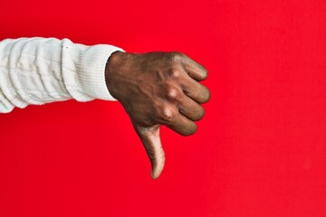 Arm and hand of african american black young man over red isolated background doing thumbs down...