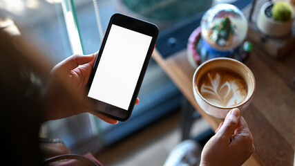 Close - up shot of Young woman holding a smartphone and coffee in a cafe.