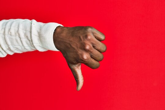 Arm and hand of african american black young man over red isolated background doing thumbs down rejection gesture, disapproval dislike and negative sign