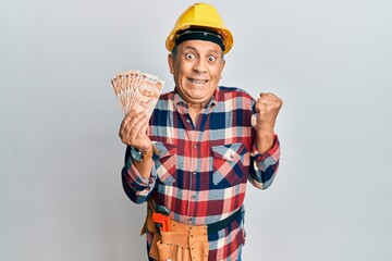 Senior hispanic man wearing handyman uniform holding turkish liras screaming proud, celebrating victory and success very excited with raised arm