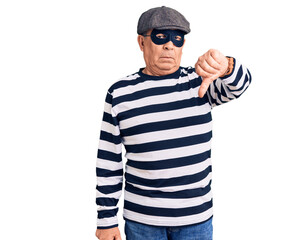 Senior handsome man wearing burglar mask and t-shirt looking unhappy and angry showing rejection and negative with thumbs down gesture. bad expression.