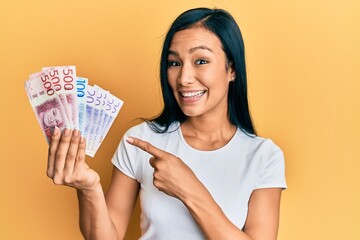 Beautiful hispanic woman holding swedish krona banknotes smiling happy pointing with hand and finger