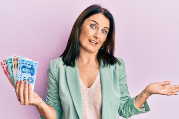 Middle age brunette woman holding yuan chinese banknotes celebrating achievement with happy smile and winner expression with raised hand