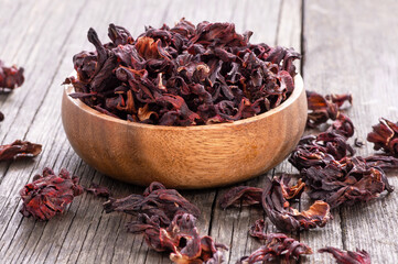 Dried hibiscus flower in wooden spoon or bowl on wooden table, alternative medicine