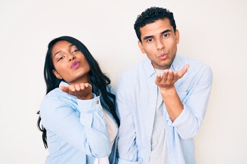 Beautiful latin young couple wearing casual clothes looking at the camera blowing a kiss with hand on air being lovely and sexy. love expression.